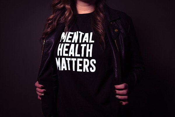Person opening black leather jacket to reveal black shirt that says "Mental Health Matters"
