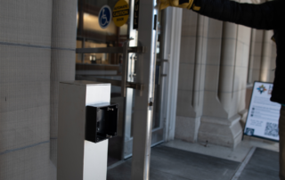 Disability Rights Montana employee holding open a door that has all the parts for an automatic door opener except for the button to activate it.
